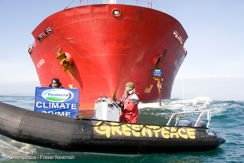 Greenpeace activists on an inflatable hold a banner reading "Climate crime", in front to the East Ambition cargo ship, while other activists are on board the ship blocking its shipment of palm kernel animal feed from Indonesia destined for Fonterra dairy farms.