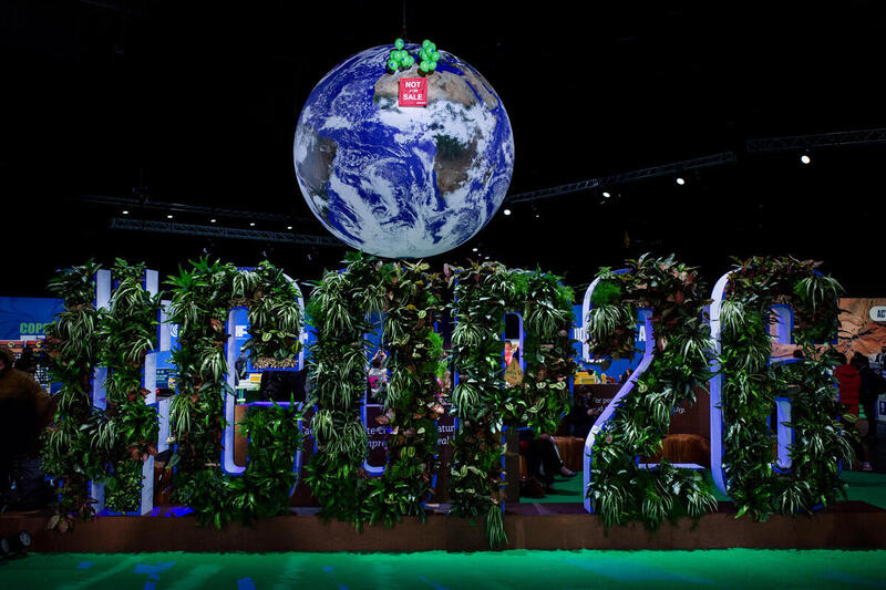 2021年11月12日，綠色和平行動者在聯合國第26屆氣候大會（COP26）場內的地球佈景裝置，升起掛有橫額的綠色氣球，展示「地球不是商品」（NOT FOR SALE）的訊息，表達制止「漂綠」和「碳抵消」的訴求。© Emily Macinnes / Greenpeace