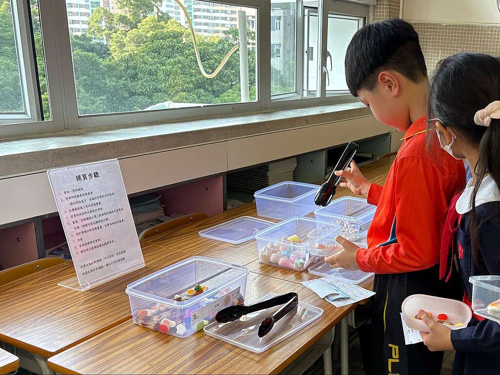 綠色和平「城市保衛隊」課程將課室化身裸買Pop-up Store，讓同學親身體驗無包裝購物，從自備容器、磅重到付款（代用幣）裸買零食，並學習計算食物碳排放。 © Greenpeace