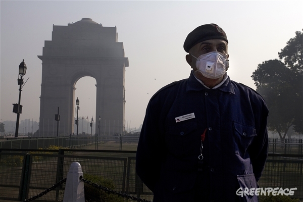 Delhi cop covered in mask stands against a hazy India Gate background