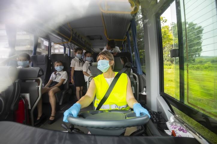 Bus driver driving school bus, wearing a face mask. Bus driver driving school bus, wearing a face mask.