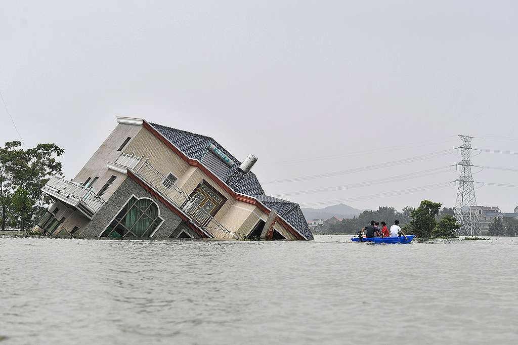Residents riding a boat past a damaged and flood-affected house near the Poyang Lake due to torrential rains in Poyang county, Shangrao city in China's central Jiangxi province. © STR/AFP via Getty Images