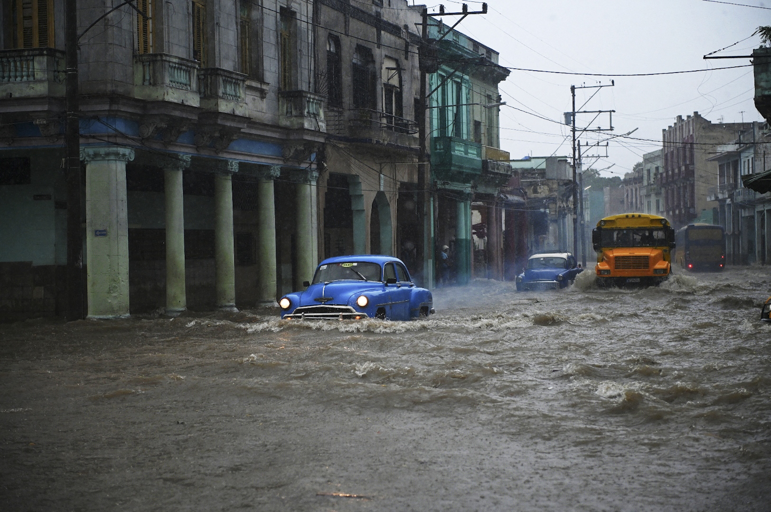 Old American cars and buses drive through a flooded street in Havana, Cuba. © Yamil Lage/AFP via Getty Images