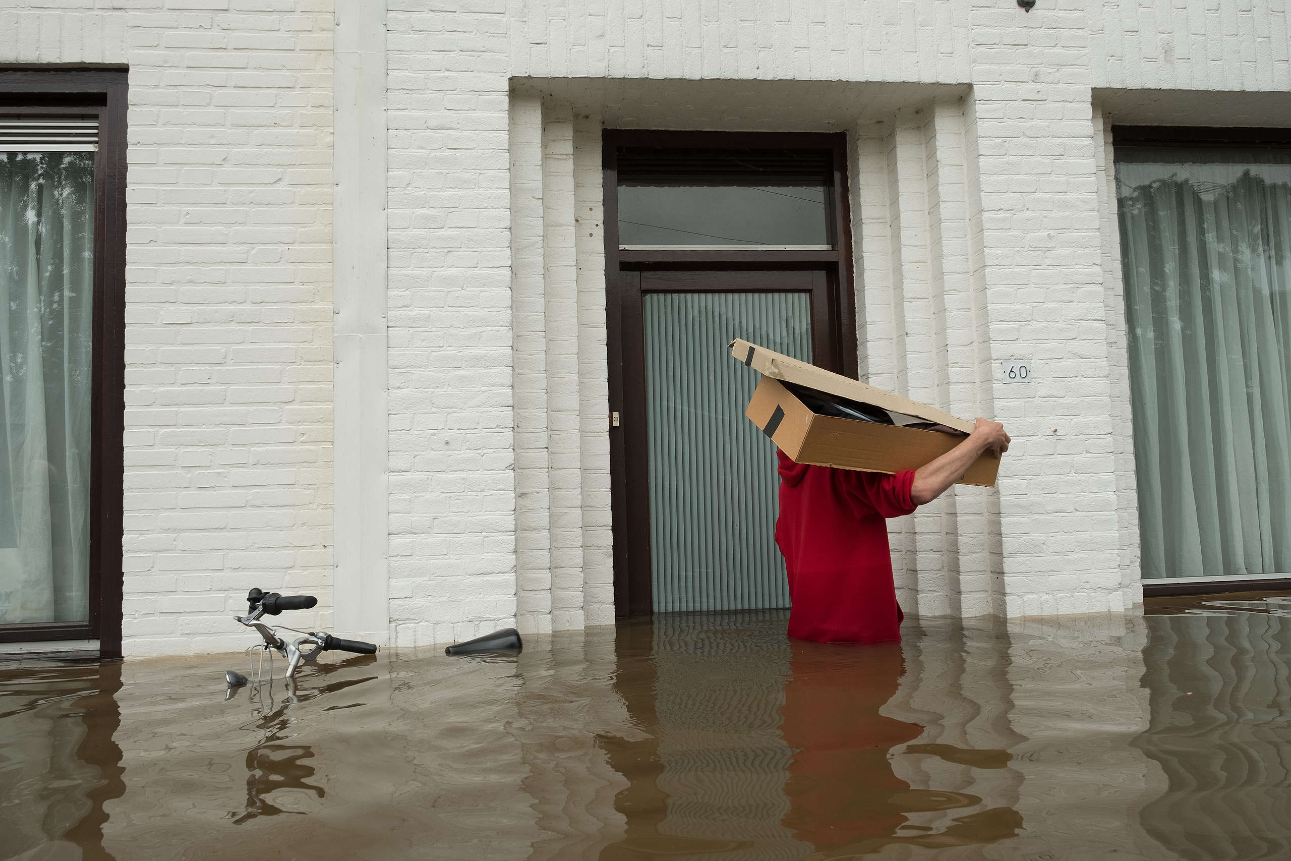 A man carries a box through a flooded street in Geulle, Netherlands. © Sanne Derks/ Getty Images
