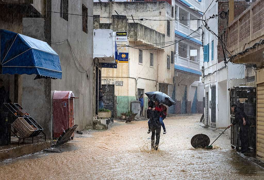 A man carries a child along a flooded street during stormy weather in Fnideq, Morocco. © Fadel Senna/AFP via Getty Images