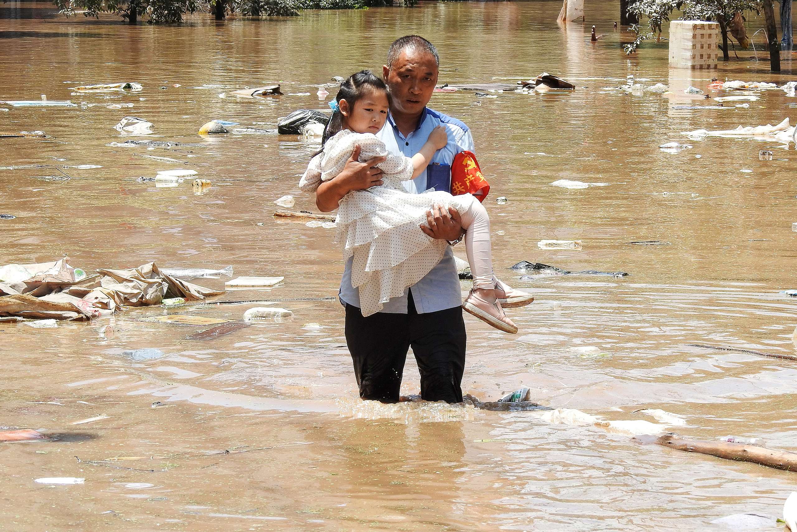 A village official evacuating a child from a flooded area following heavy rains in Dazhou, China. © STR/AFP via Getty Images