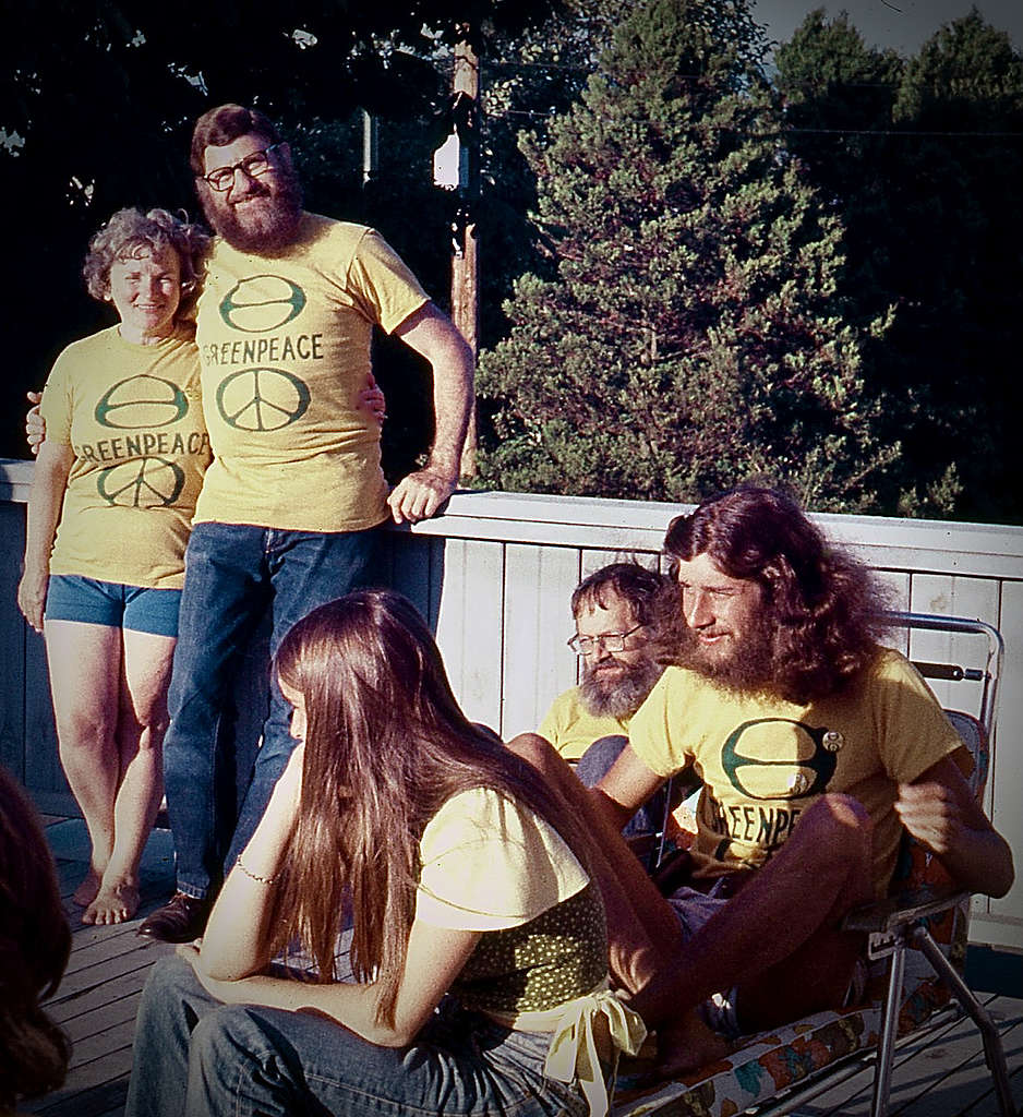 Dorothy and Irving Stowe stand together outside, with Bree Drummond, Jim Bohlen, and Rod Marining nearby in 1971. All wear yellow and green Greenpeace T-shirts.