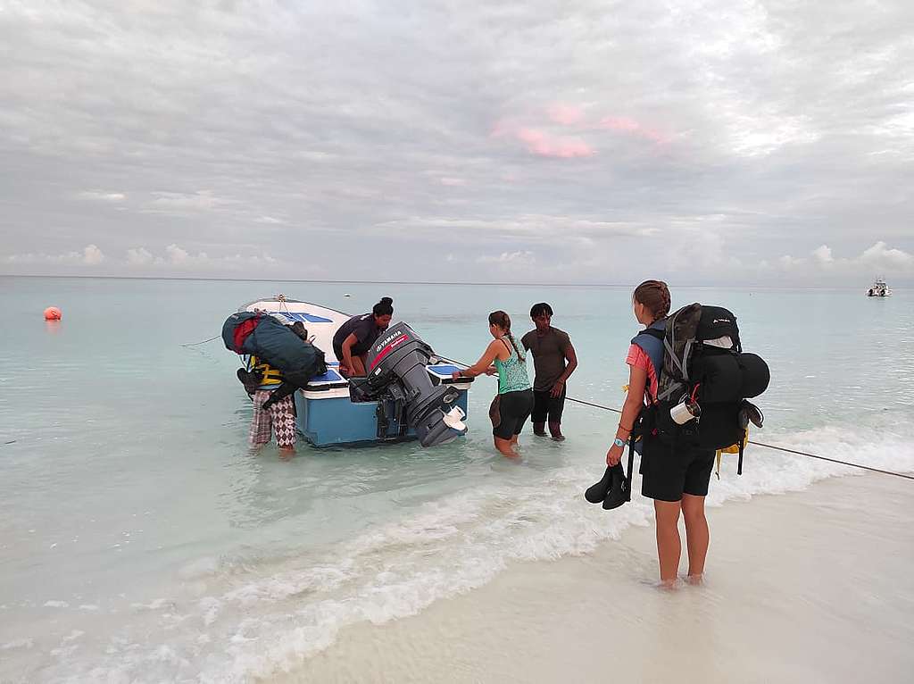 A group of young people on the beach, in bright and brown shirts, bring in a blue and white boat. © Emma Mederic A group of young people on the beach, in bright and brown shirts, bring in a blue and white boat. © Emma Mederic