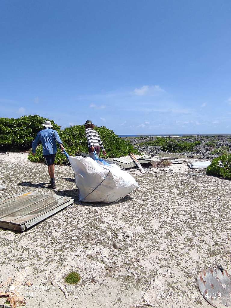 Two people, in long sleeve shirts, blue and striped, pull large white bags over sand. © Emma Mederic Two people, in long sleeve shirts, blue and striped, pull large white bags over sand. © Emma Mederic