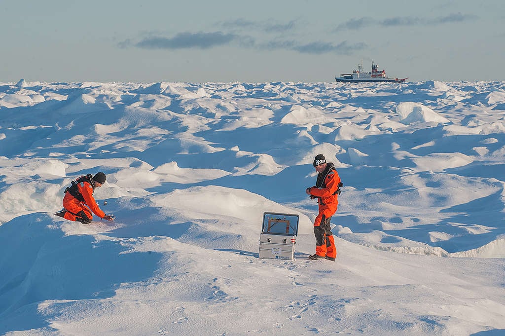 On a stretch of Arctic land completely covered in snow, two people are collecting snow samples.