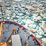 A drone shot of a US Coast Guard ship with men on deck is in Beaufort Sea with floating ice chunks.