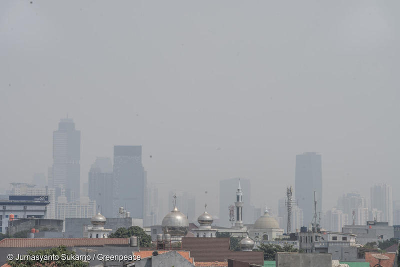A mosque, houses and in the background tall buildings are covered by smog from air pollution in Jakarta