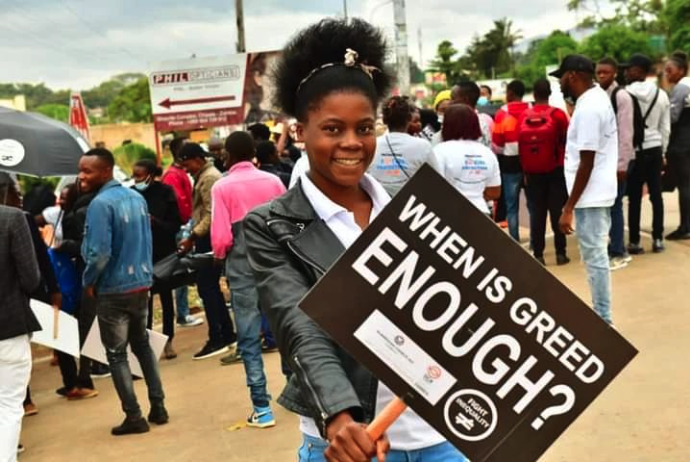 Fight Inequality activist Beatah Phiri in Chipata, Zambia holding a sign that reads: When is greed enough?