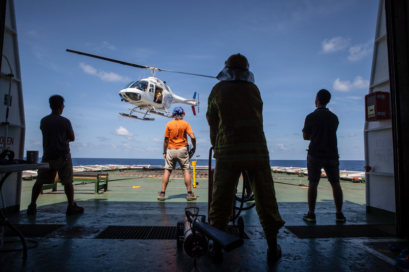 Crew members watch a helicopter taking off from the helideck of the Esperanza