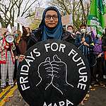 A girl wearing a head scarf holding a placard that says Fridays For Future MAPA. Behind her are other young people at the strike.