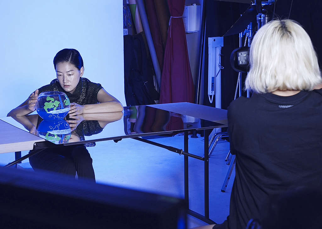 A woman with blonde hair with a camera pointing at another woman sitting on a table