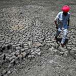Shivaram, a villager walking through the cracked bottom of a dried-out pond on a hot summer day at Bandai village in Pali district. - Every day dozens of villagers, mostly women and children, wait with blue plastic jerry cans and metal pots for a special train bringing precious water to people suffering a heatwave in India's desert state of Rajasthan. ©PRAKASH SINGH/AFP via Getty Images.