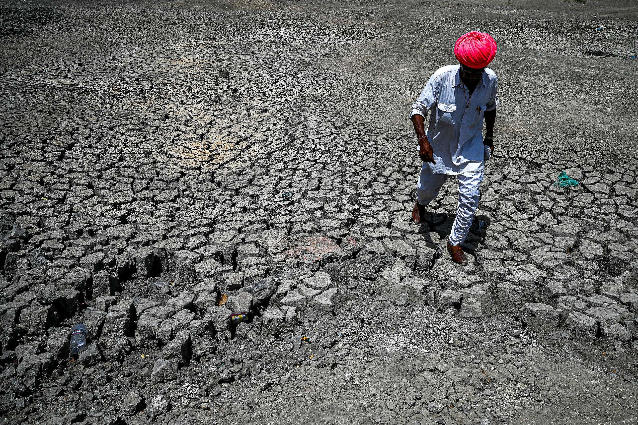 Shivaram, a villager walking through the cracked bottom of a dried-out pond on a hot summer day at Bandai village in Pali district. - Every day dozens of villagers, mostly women and children, wait with blue plastic jerry cans and metal pots for a special train bringing precious water to people suffering a heatwave in India's desert state of Rajasthan. ©PRAKASH SINGH/AFP via Getty Images.