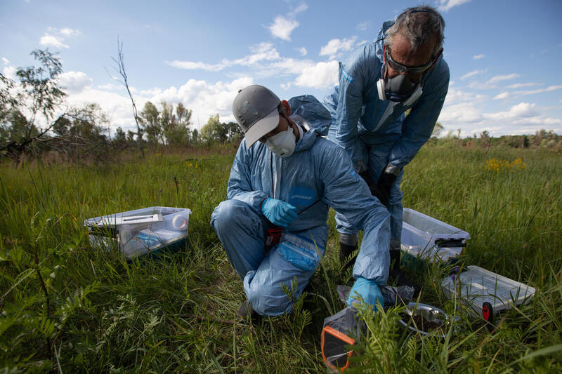 Two radiation investigators in blue protective suits and masks collect samples