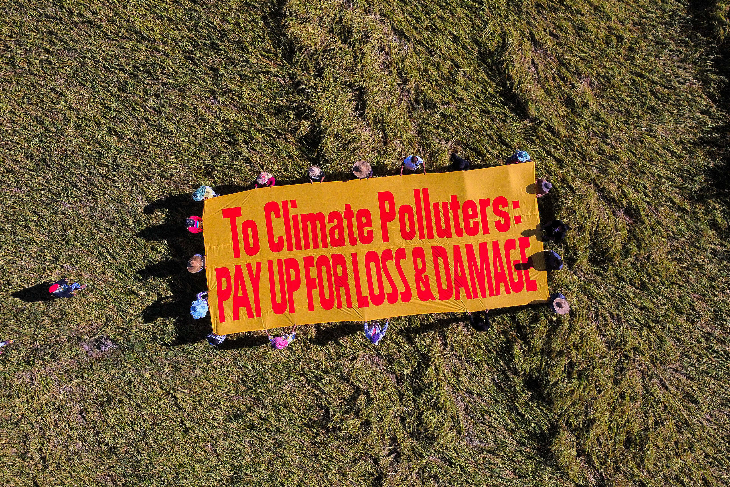 People holding a huge banner saying: "To climate polluters: pay up for loss and damage"