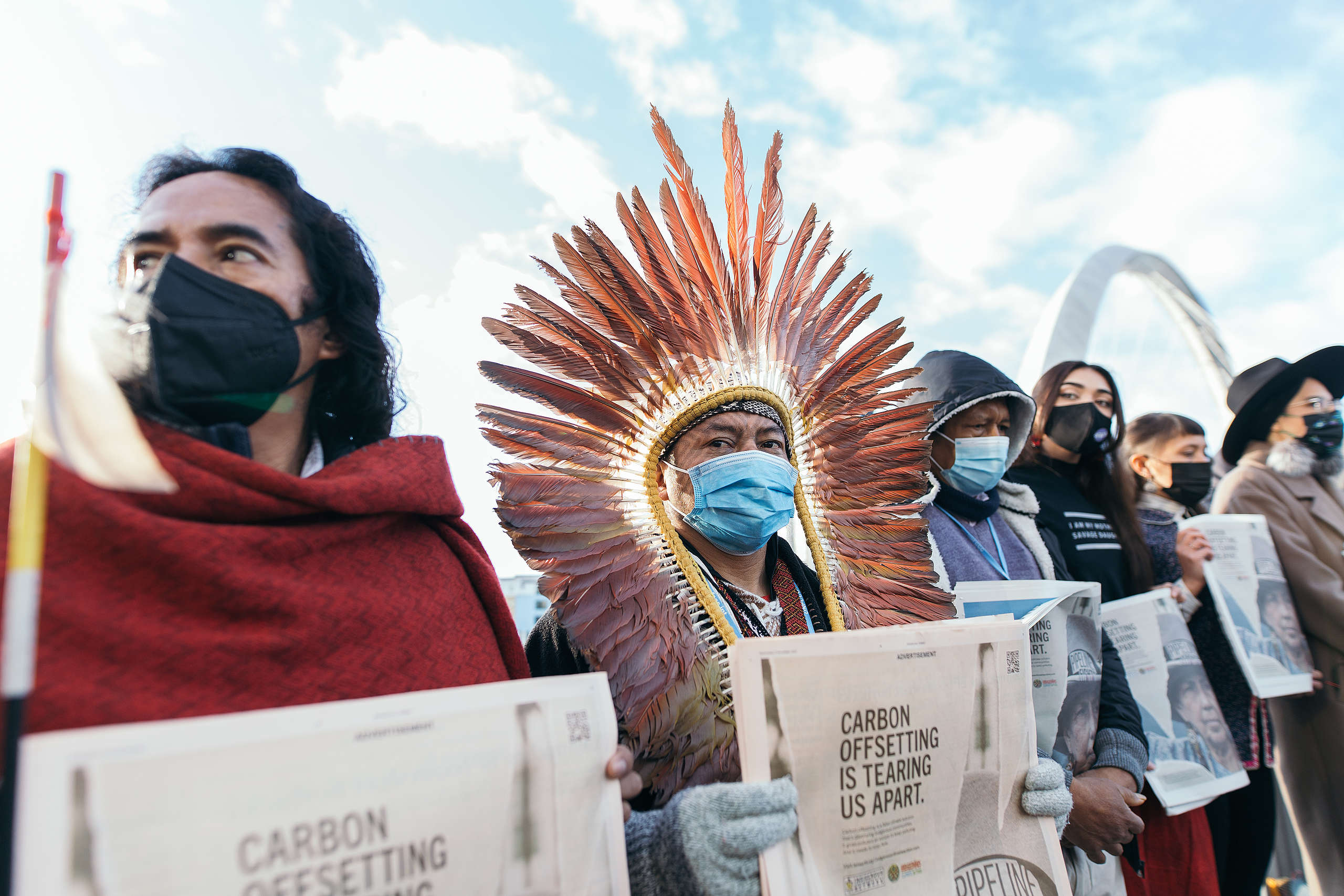 Indigenous environmental activists, one with a traditional headdress hold placards protesting false climate / nature solutions at COP15.
