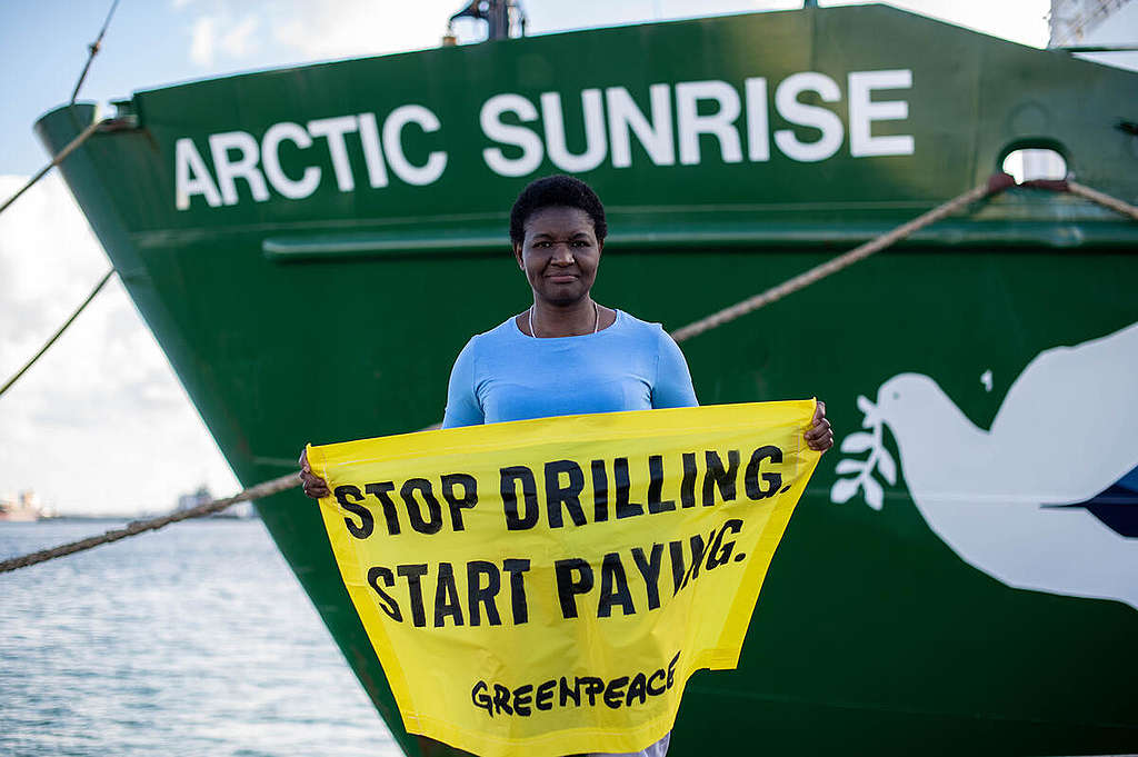 Victorine Che Thöner, spokesperson from Germany and originally from Cameroon in Las Palmas, Gran Canaria. Victorine is holding a hand banner that reads 'Stop Drilling. Start Paying.'