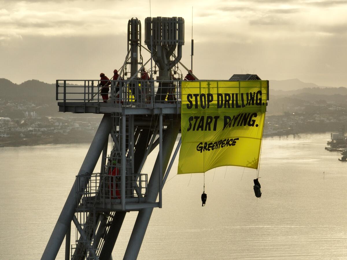 Protestors atop a platform’s 125m high flare boom waving a banner saying ‘Stop drilling. Start Paying.’