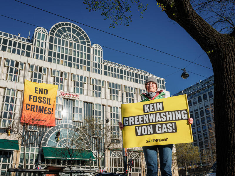 Climbers from Greenpeace Central and Eastern Europe hang a six-by-eight-metre banner reading "End Fossil Crimes" on the European Gas Conference venue in Vienna. (the Vienna Marriott Hotel) in protest against the fossil fuel industry’s plans to “future-proof gas” in the face of climate disaster. Greenpeace is calling for fossil fuel companies to stop their climate-wrecking activities and be held accountable for their crimes. Woman holds banner in the foreground to protest industry greenwashing.