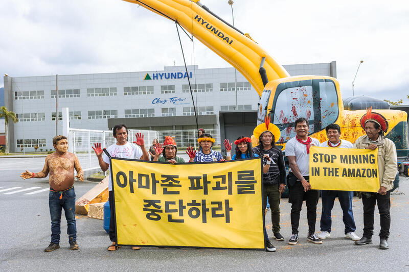 Greenpeace Brazil activists and Indigenous leaderships hold a peaceful action at the gates of a Hyundai plant in Itatiaia, Rio de Janeiro state, standing next to an inflatable excavator and holding the messages "Amazon free of illegal mining", "Stop the excavators" and "Out, illegal mining".
