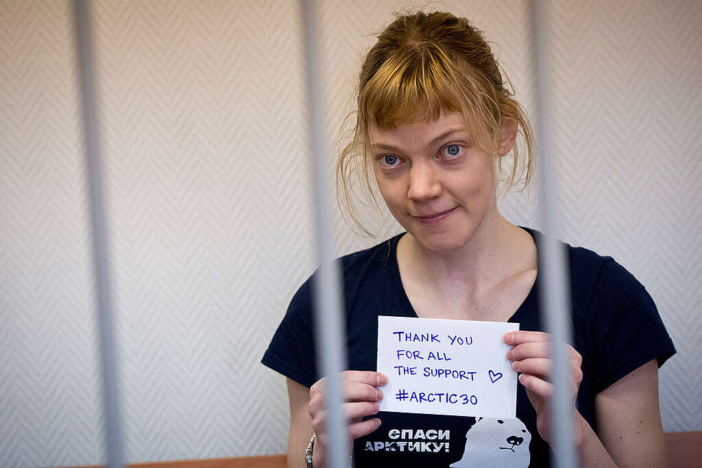 Sini Saarela pictured behind bars at a bail hearing at a court in Murmansk, Russia holds a small handwritten note saying 'Thank you for all your support. #Arctic30'. © Greenpeace