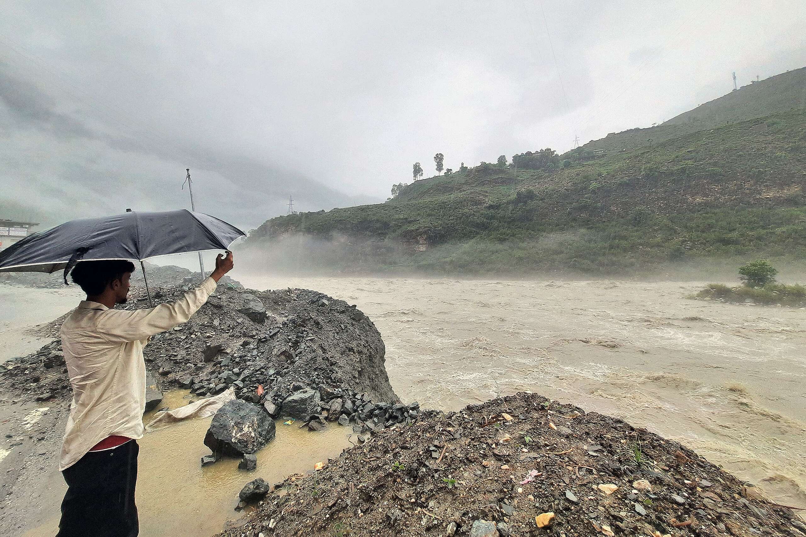 A man holds an umbrella while standing on the banks of swollen river Satluj after heavy monsoon rains in Rampur, in India's Himachal Pradesh state. © AFP via Getty Images