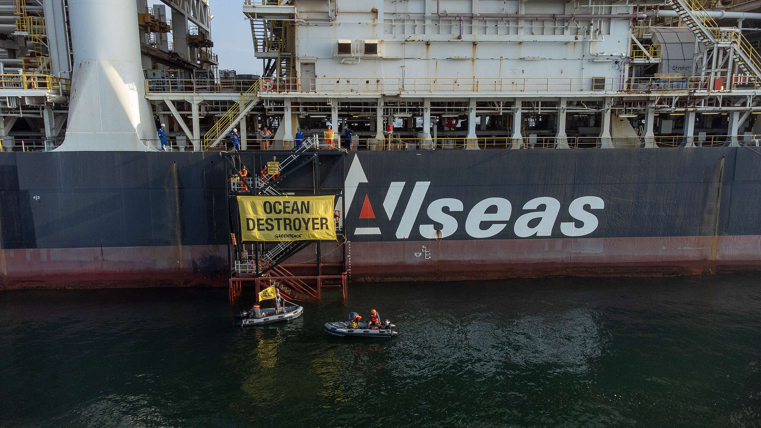 Activist in small boats hold up yellow banner in front of mining ship