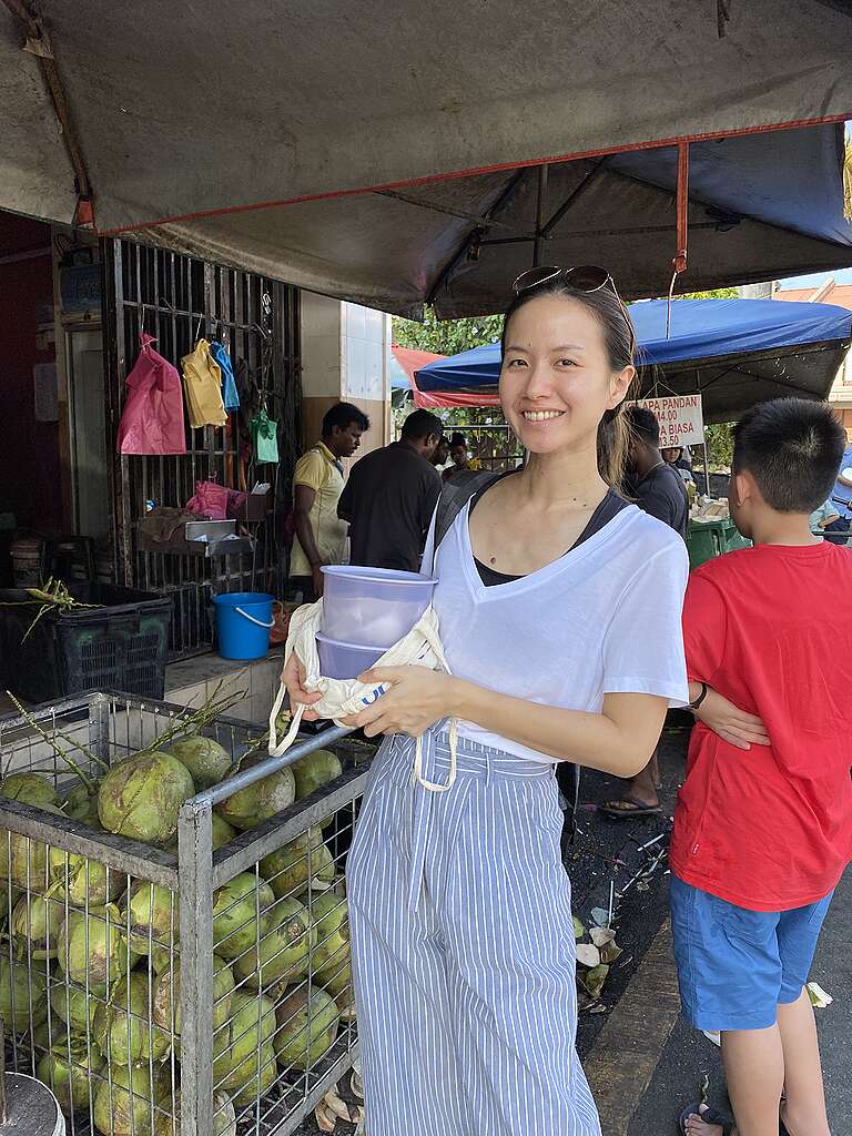 A woman holding reusable food containers and an eco bag in front of a market stall