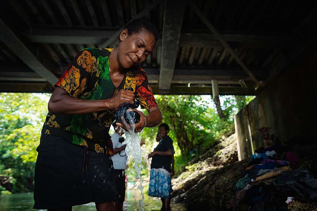 A woman hand washing clothes at a river.