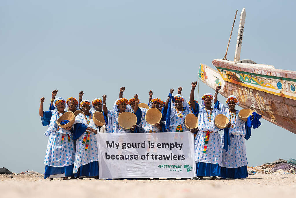 Women activists with their empty traditional calabash bowls, raise their fists in defiance in Mbour, Senegal to highlight their grassroots campaigns against industrial overfishing and coastal industrialisation and demand government action. They also hold a banner reading "My gourd is empty because of trawlers". © Clément  Tardif / Greenpeace