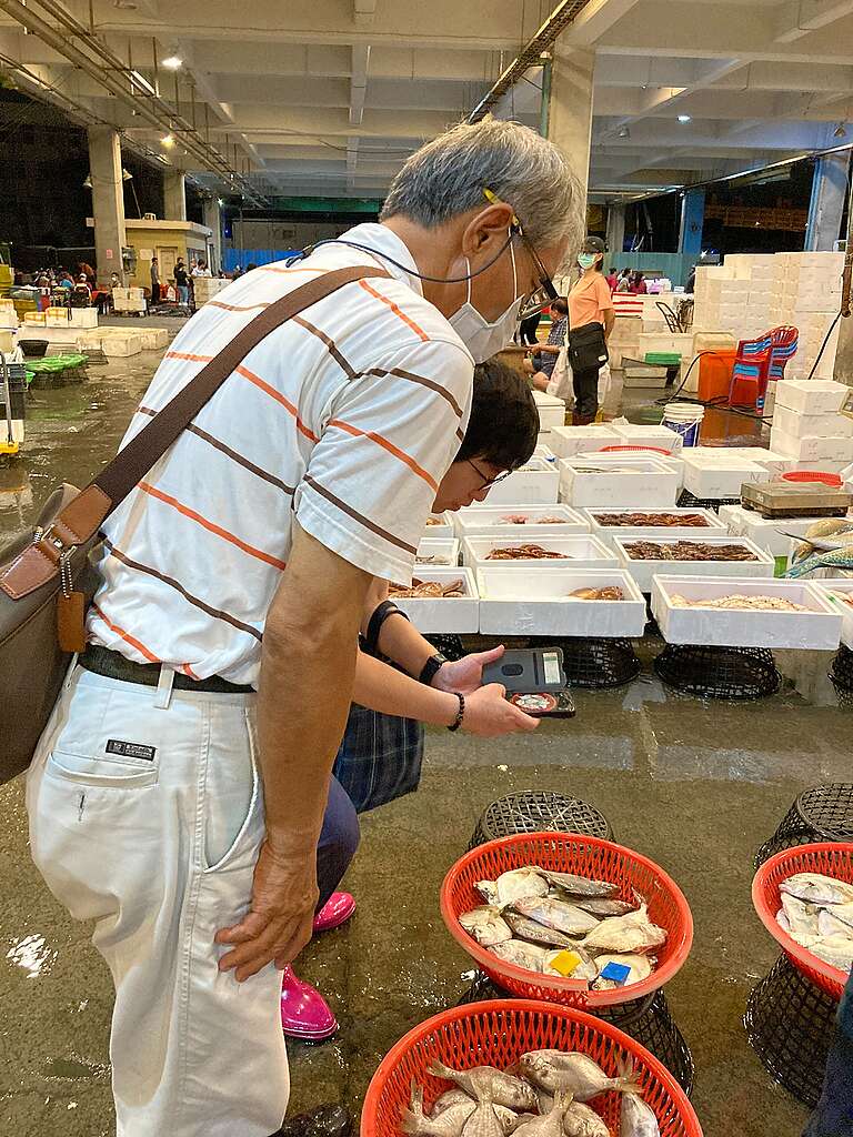 An elderly man bending over a plastic basket full of fish