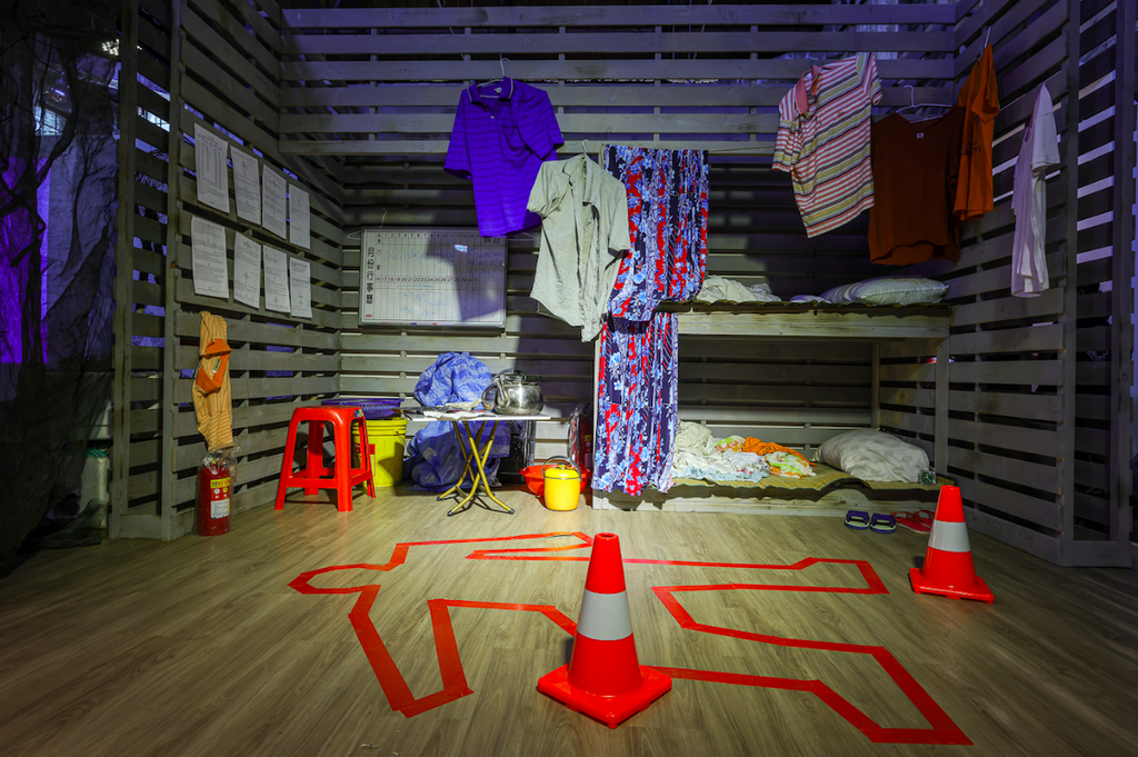A room with clothes hanging off a bunk bed and orange cones on the floor next to a body outline created using tape