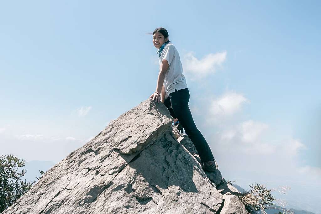 A young woman smiling on top of a large rock a young woman on top of a rock