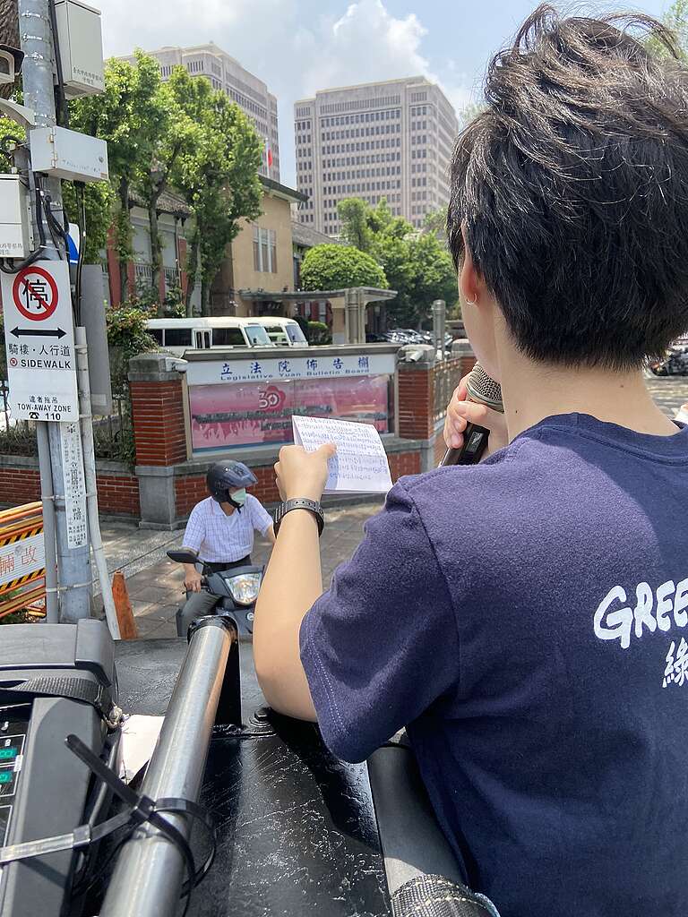 A woman holding a microphone is speaking out in the public on top of a vehicle