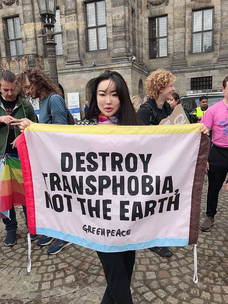 A woman is holding a banner that says "Destroy Transphobia, Not The Earth" on the street
