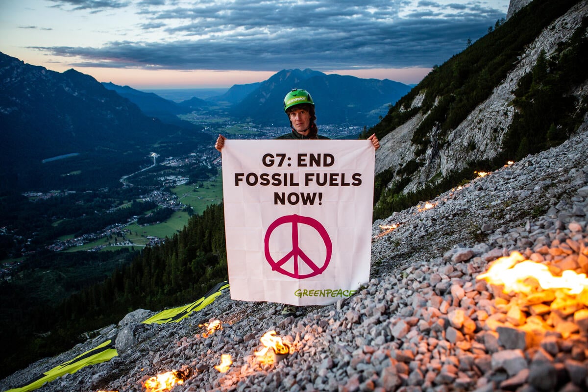On the Waxenstein mountain, an activst holds a banner that reads "G7: Stop Gas, Oil and Coal Now."