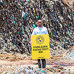 Greenpeace Africa volunteer with a sign reading "Strong Global Plastics Treaty Now!" at the heart of the Dandora dumpsite. As vast stretches of land are swallowed by discarded plastics, it underscores the urgency of our call: a reduction in plastic production by 75%.