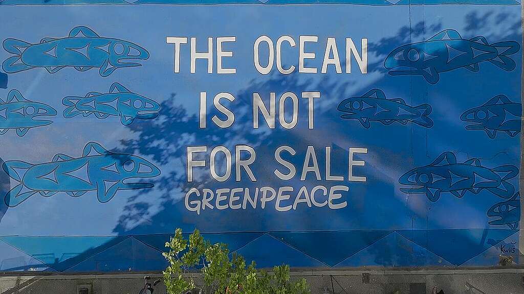 A ground mural with the phrase 'The Ocean is not for Sale - Greenpeace', written on a blue background and surrounded by fish