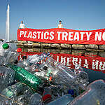 Activists hold up a banner saying "Plastics Treaty Now" in front of the Jet d'Eau of Geneva.