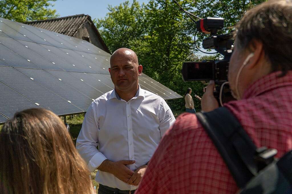 The Mayor of Chortkiv, Ukraine, Volodymyr Shmatko, gives an interview with solar panels in the background.