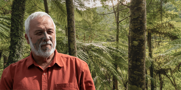 Mike Smith, a gray-haired man with a beard wearing a rust-red button-up shirt, stands in a lush forest surrounded by tall trees and large green ferns Mike Smith, a gray-haired man with a beard wearing a rust-red button-up shirt, stands in a lush forest surrounded by tall trees and large green ferns