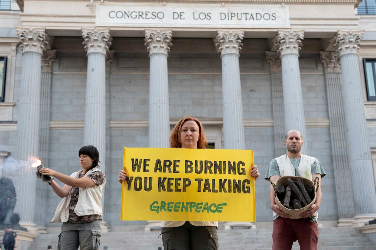 Artificial smoke, ashes, burnt logs and a black banner outside the Congress of Deputies reading 