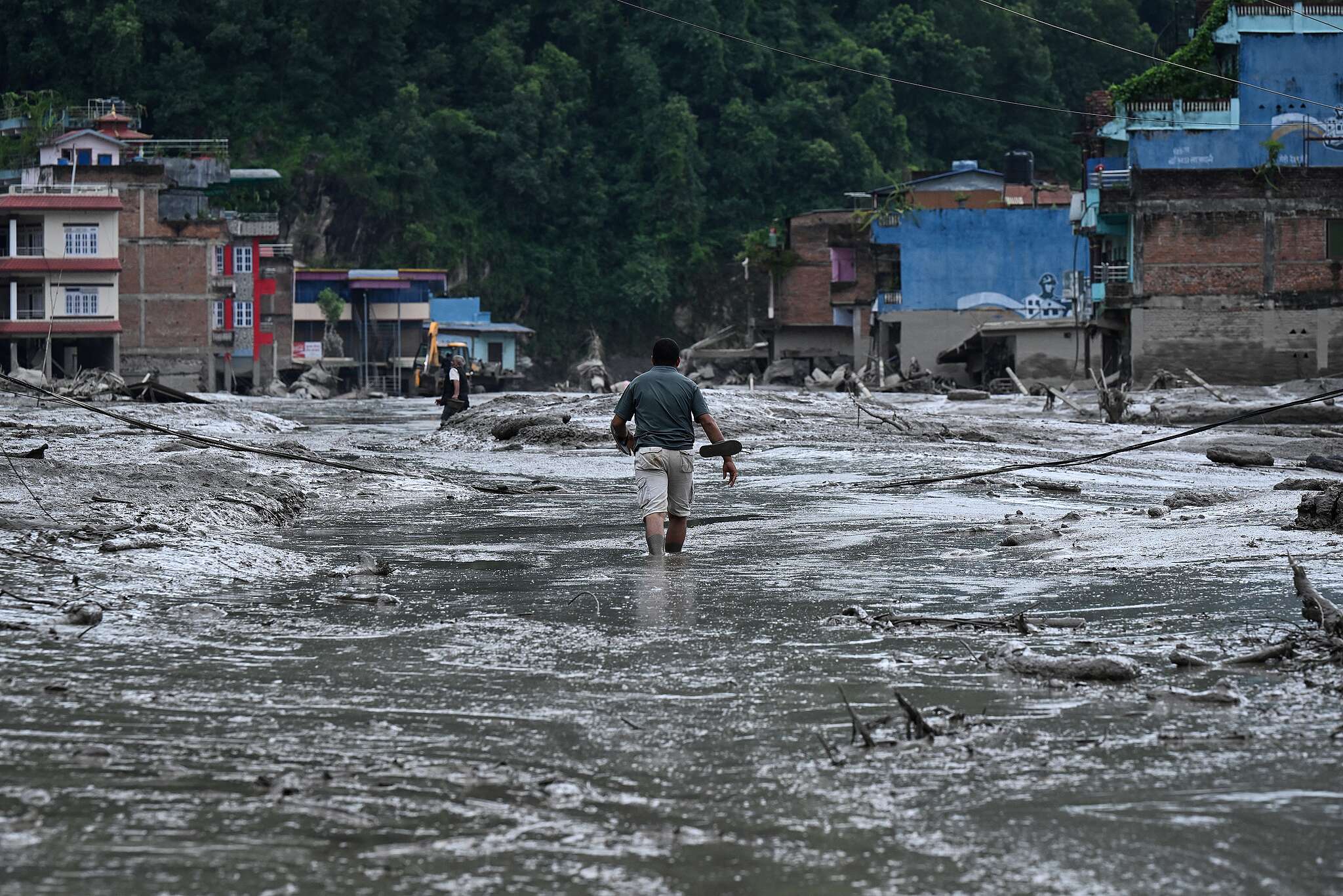 A resident walks along a street covered in mud following flash floods and a landslide disaster in Devighat, in Nepal's Nuwakot district on August 26, 2026. A massive flood and landslide disaster on the Nepal-Tibet border killed at least 103 people on August 26, 2026 and left several hundred missing, many of them foreign tourists. Aid workers said entire settlements had been "wiped out". Some 403 tourists -- 341 of them foreigners -- were unaccounted for several hours after the disaster struck, according to the tourism ministry.