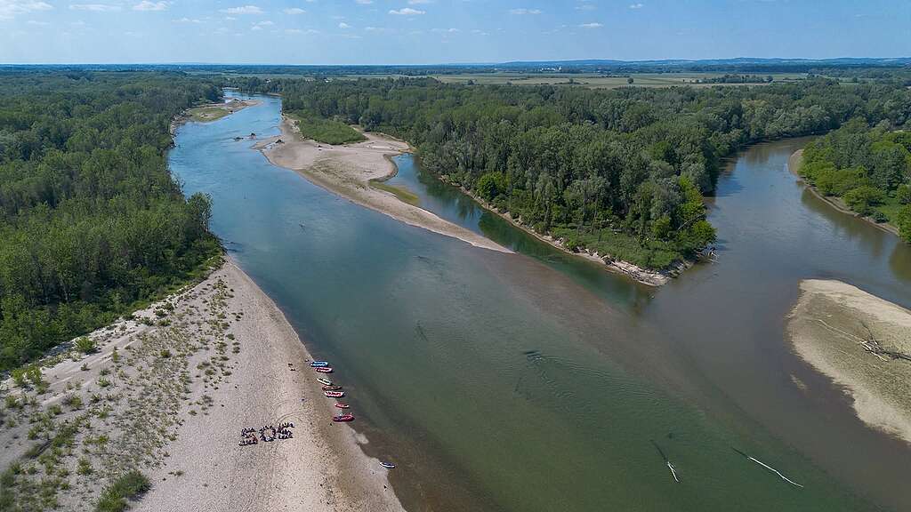 Confluence of Mura and Drava Aerial view of the Mura and Drava rivers meeting amid forested riverbanks, sandy islands, and gravel bars, with kayaks gathered along the shore spelling out SOS