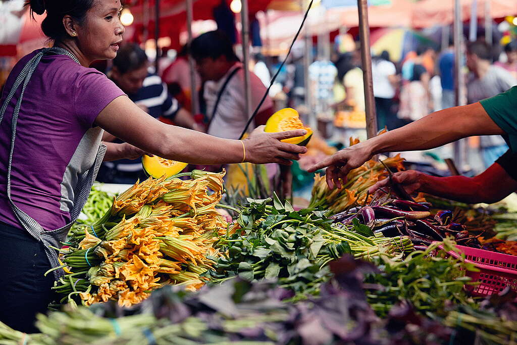 A seller in a traditional marker, handing a fruit to a shopper